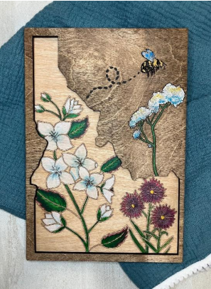 Idaho Wildflower is a layered wood paint by numbers style canvas with stained wood and acrylic paint showing Idaho state flower the syringa. There are also other wildflowers with a bee